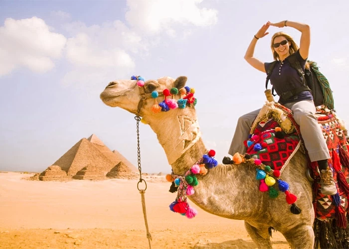 a female tourist riding a camel in front of the Pyramids of Giza }}